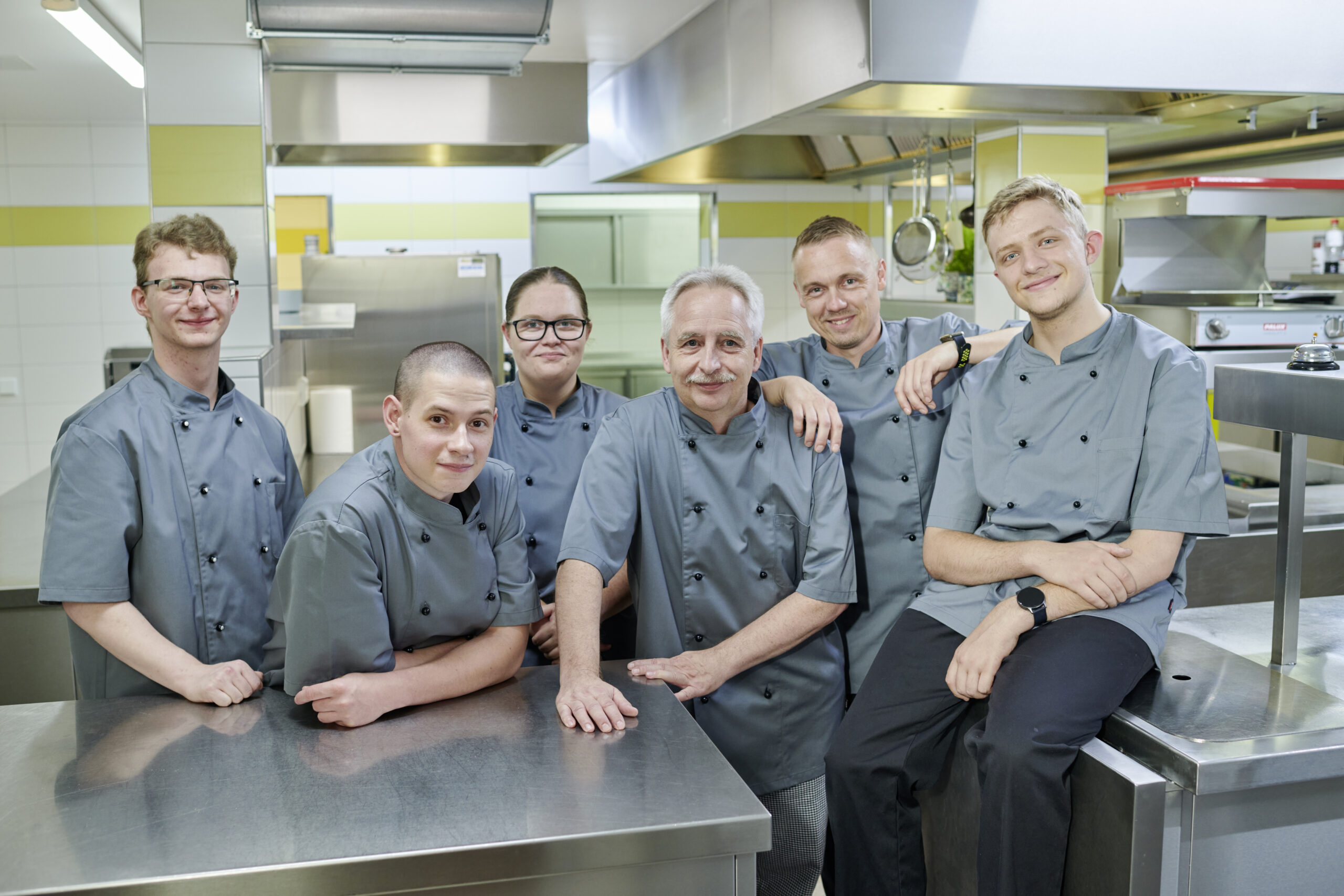 Küchenteam des Parkhotel Neustadt hat sich in der Hotelküche versammelt und lächelt in die Kamera.